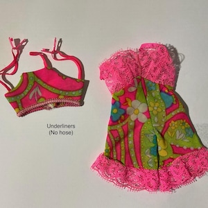 May include: A doll-sized outfit consisting of a pink and green floral patterned top with thin straps and a matching dress featuring a pink lace bodice and hem. The text "Underliners (No hose)" is printed below the top piece of the clothing set.