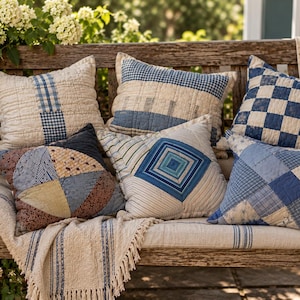 May include: A collection of six square throw pillows featuring various blue and white patchwork, quilted, and geometric patterns. The pillows display diverse designs including checkered, striped, and diamond motifs, all crafted with visible stitching.