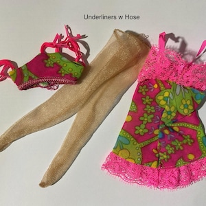 May include: A set of doll clothing labeled Underliners w Hose, featuring a pink and green floral patterned top with bright pink straps, a pair of sheer beige pantyhose, and a matching pink and green floral dress with bright pink lace trim.