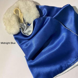 May include: A midnight blue satin cape featuring a white faux fur collar and a light-colored plastic hanger. The garment has a smooth, reflective surface and a white lining visible at the edges. The text Midnight Blue is printed on the left.