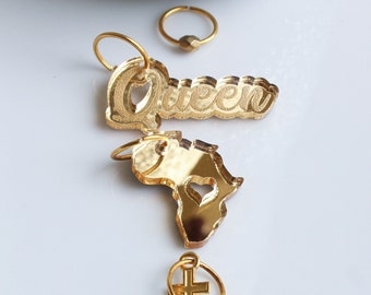 Puede incluir: Un conjunto de siete piezas de joyería doradas, que incluye un dije con la palabra "Queen", un dije con forma del continente africano con un corazón recortado, un dije con una cruz y cuatro aretes de aro con diferentes dijes.