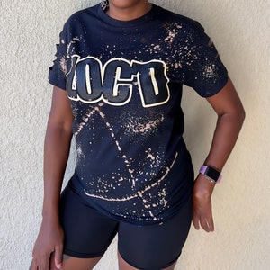 May include: Black t-shirt with a bleach-splattered design and the word "LOCTD" in gold lettering.