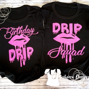 May include: Two black t-shirts with pink glitter text and a pink glitter lip design. The text on the first shirt says "Birthday Drip" and the text on the second shirt says "Drip Squad".