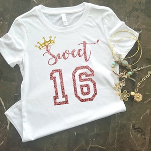 May include: White t-shirt with a gold crown and the words "Sweet 16" in pink glitter.