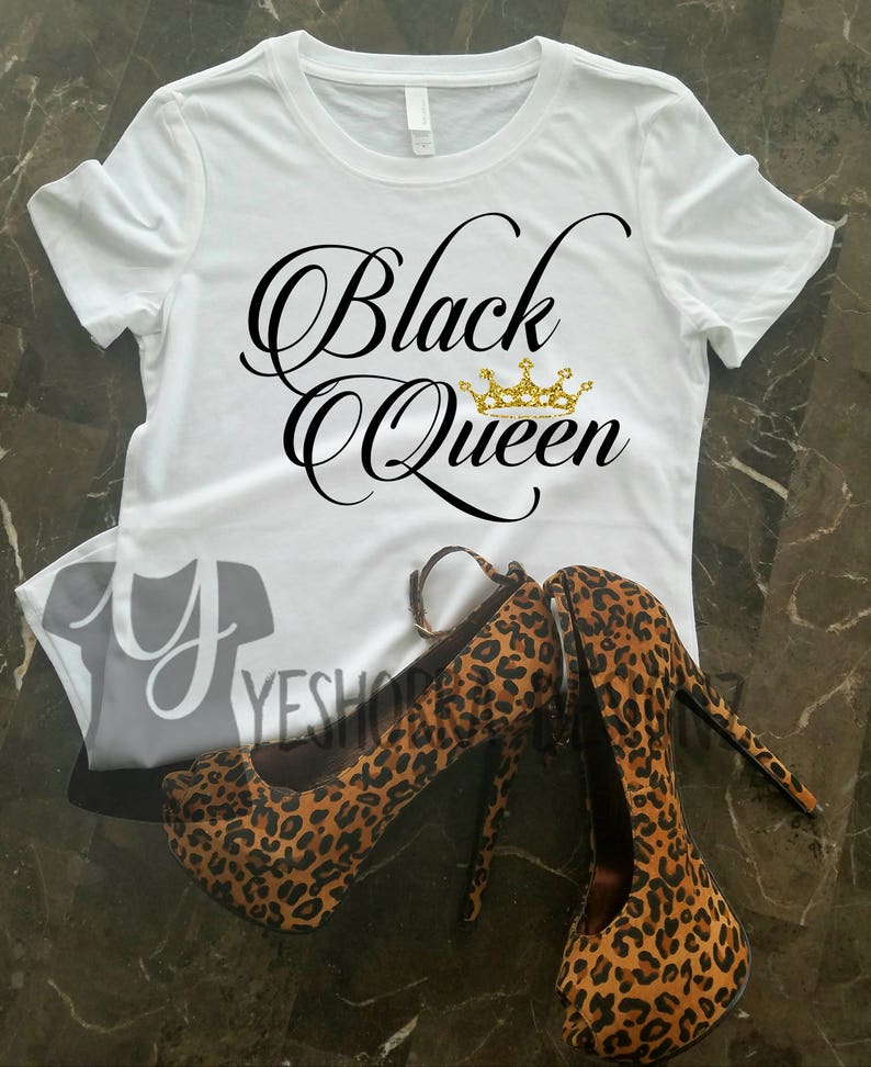 May include: White t-shirt with the text "Black Queen" in black script with a gold crown above the word "Queen".