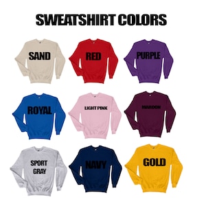 May include: A display of nine crewneck sweatshirts in various colors, including sand, red, purple, royal blue, light pink, maroon, sport gray, navy, and gold. Each sweatshirt has the color name printed in bold black letters.