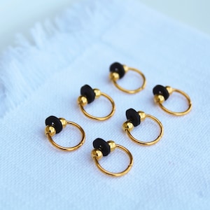 May include: Six gold hoop earrings with black beads. The hoops are small and delicate.