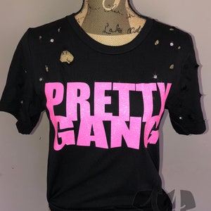 May include: Black t-shirt with distressed detailing and a pink glitter graphic that reads "PRETTY GANG".