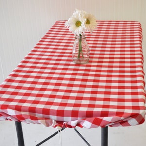 May include: Red and white checkered tablecloth with a white flower arrangement in a clear glass vase in the center.