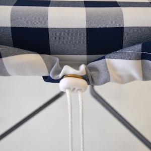 May include: A white and navy blue checkered tablecloth with a white drawstring and a white plastic toggle. The tablecloth is gathered around a black metal table leg.