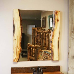 May include: A rectangular mirror with a natural wood frame. The frame is made of two thick pieces of wood with a rough, bark-like texture. The mirror is reflecting a room with wooden furniture.
