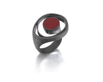 May include: A silver ring with a red circular stone set in a swirling design.