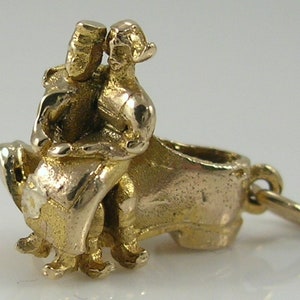 May include: Gold charm depicting a couple riding a turtle. The charm is detailed and has a textured finish.