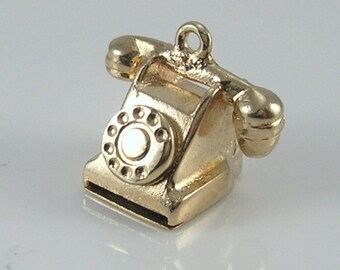 May include: A gold charm in the shape of a vintage rotary phone. The phone has a black dial and a gold receiver.