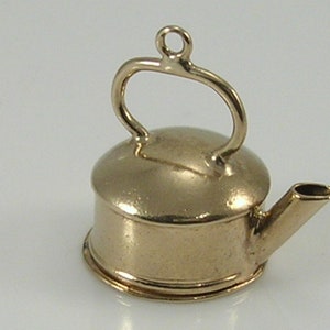 May include: A gold-colored metal charm in the shape of a teapot. The teapot has a round body, a curved handle, and a spout.