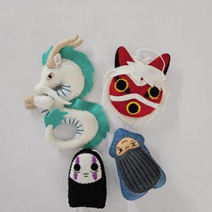 May include: Four felt ornaments featuring characters from a popular animated film. The ornaments include a white and teal dragon, a red and white mask, a black and white figure, and a blue figure with a gray blanket.