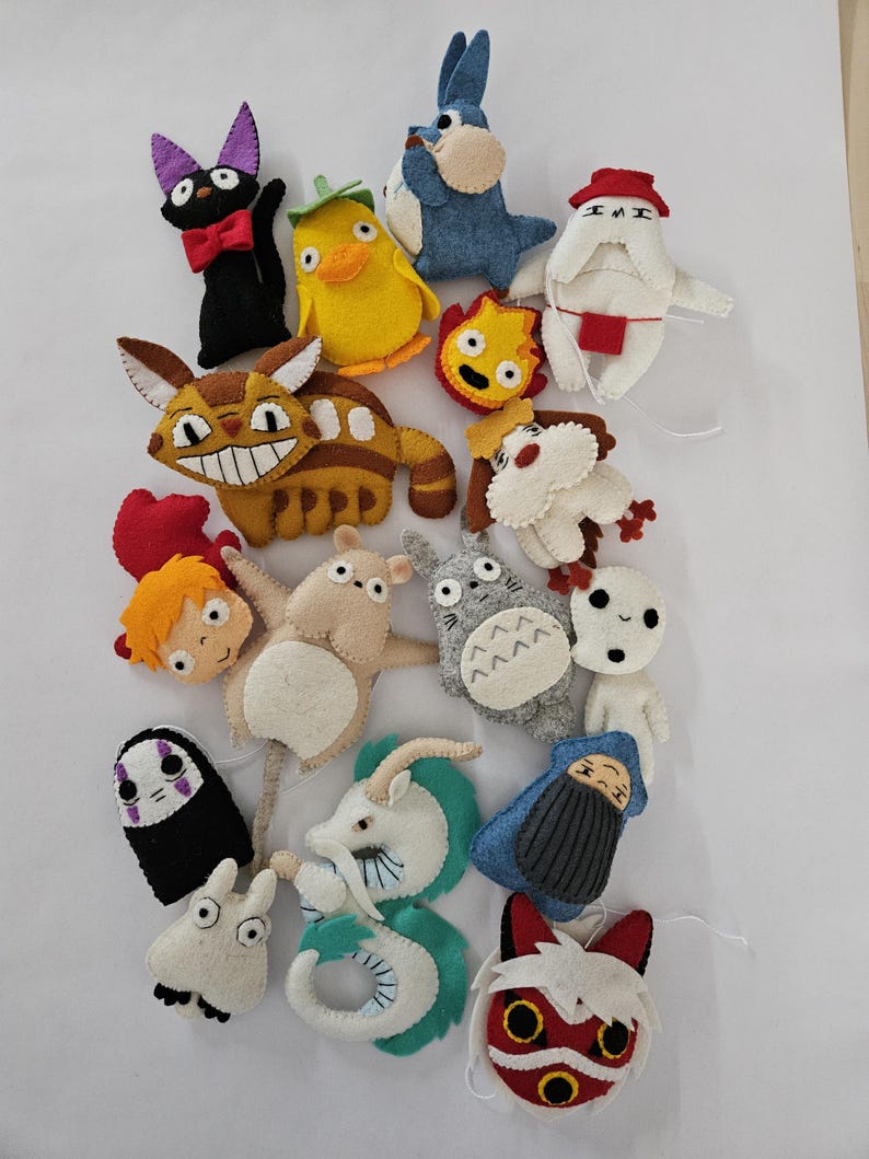 May include: A collection of colorful felt character plushies, including a black cat with a red bow tie, a yellow duck, and a blue rabbit. Other characters include a brown and tan creature with a large grin, and a gray creature with a white belly.