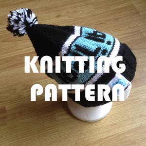 May include: Black and white knit beanie with a blue and white stripe and a pom pom on top. The beanie has the word "Knitting Pattern" written on it.