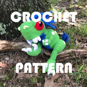 May include: Crochet pattern for a green and blue dinosaur with a red eye. The dinosaur is sitting on a branch with the text "CROCHET PATTERN" above it.