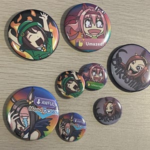 May include: A collection of colorful anime-style button pins. The pins feature various characters with emotive expressions and text like "Umazed!" and "Awful Mood Down." The designs include vibrant colors and detailed artwork.