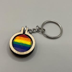 May include: A rainbow-colored embroidery design on a wooden keychain with a silver key ring.