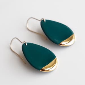 Può includere: Un paio di orecchini a forma di lacrima con una finitura smaltata verde blu scuro e un accento dorato sul bordo inferiore.