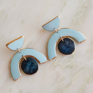 Könnte beinhalten: Ein Paar blaue und goldene geometrische Ohrringe mit einem schwarzen Kreis in der Mitte jedes Ohrrings.