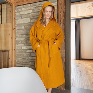 May include: A mustard yellow hooded robe with long sleeves, a tie waist belt, and two front patch pockets. The garment features a wrap-front design and a large hood. The text THE LINEN VALLEY is visible in the upper right corner of the image.