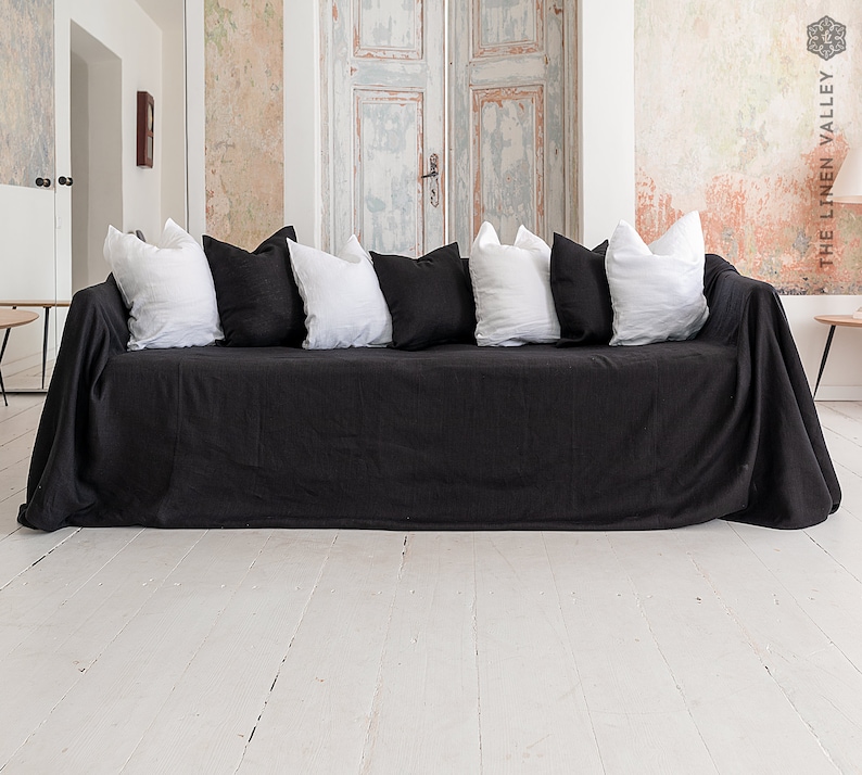 May include: A charcoal black linen sofa cover draped over a couch, featuring a series of alternating solid white and solid black square throw pillows arranged along the backrest. The fabric has a visible woven texture and hangs down to the floor.