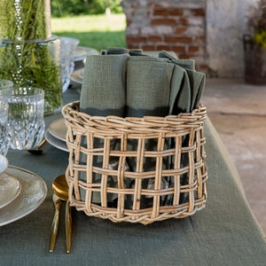 May include: A wicker basket filled with folded green linen napkins on a green linen tablecloth. The basket is on a table with a glass jug and glasses.