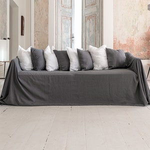 May include: A dark gray sofa cover draped over a couch, featuring a series of alternating white and dark gray square throw pillows arranged along the backrest. The fabric has a visible texture and hangs down to the floor on both sides of the sofa.