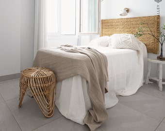 May include: A white bed with a woven headboard and a tan throw blanket. A woven stool sits next to the bed.
