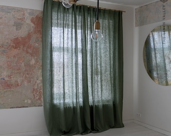 May include: A pair of green linen curtains hang in a room with white walls and a round mirror. The curtains are made of a natural fabric and have a relaxed, casual look.