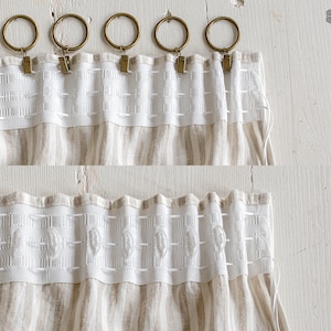 May include: Close-up of a beige and white striped linen curtain with a white decorative trim. The curtain is hung on a rod with five gold rings and clips.