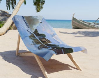 May include: A wooden beach chair with a blue and white patterned fabric. The chair is set on a sandy beach with a view of the ocean and a boat in the background. The chair is made of light-colored wood.