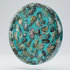 May include: A circular tray made of clear resin with a vibrant turquoise tint, embedded with numerous iridescent abalone shell fragments. The shell pieces display a variety of natural colors including green, blue, and pearlescent tones, suspended throughout the transparent material in a scattered pattern.