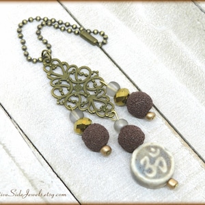 May include: A brown and gold car charm with a filigree design, brown beads, and a ceramic charm with the Om symbol.