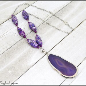 May include: A purple agate pendant necklace with a silver chain and purple and silver patterned beads.