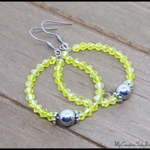 May include: A pair of hoop earrings with silver metal accents and bright yellow beads.