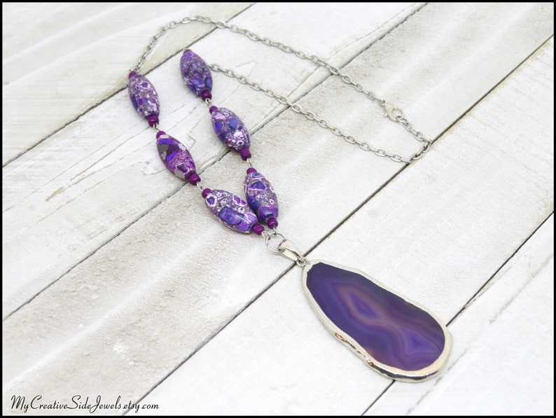 May include: A purple agate pendant necklace with a silver chain and purple and silver patterned beads.