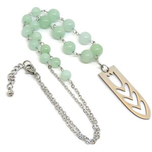 May include: A silver chain necklace with a silver pendant featuring a cut-out design of three tulips. The necklace is strung with light green beads.
