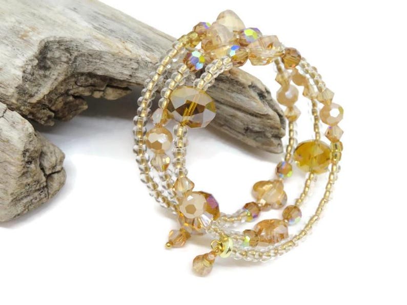 Puede incluir: Una pulsera de m&uacute;ltiples hilos con cuentas doradas y transparentes. La pulsera presenta cuentas de varios tama&ntilde;os y formas, incluidas cuentas facetadas y redondas. Las cuentas est&aacute;n ensartadas en un alambre de color dorado. La pulsera se exhibe sobre una superficie blanca con un trozo de madera flotante.