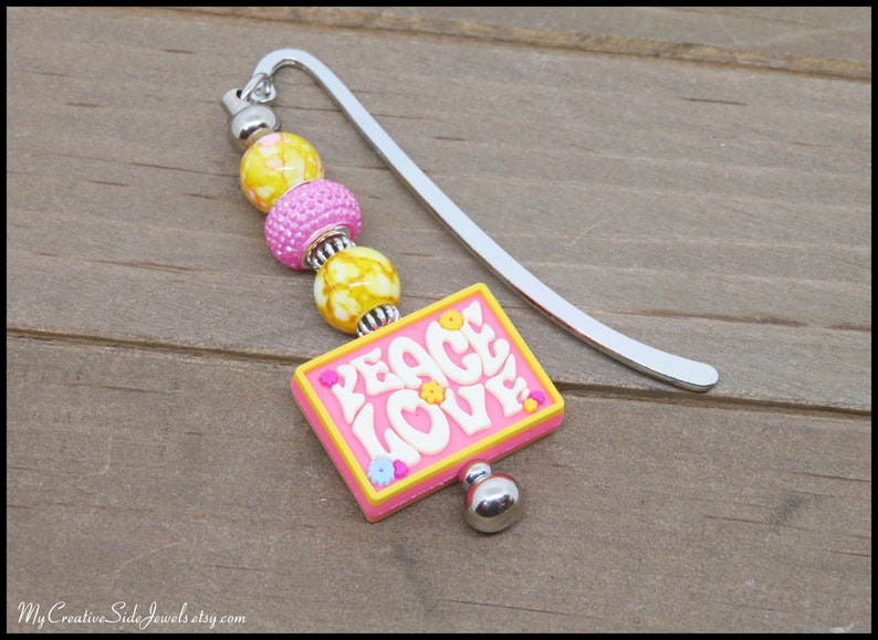May include: A silver bookmark with a pink and yellow beaded charm that says "Peace Love".