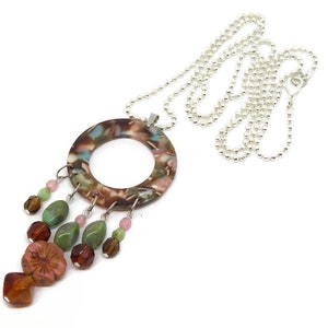 May include: A brown, green, and pink necklace with a round pendant and a silver chain. The pendant has a floral pattern and is accented with beads.