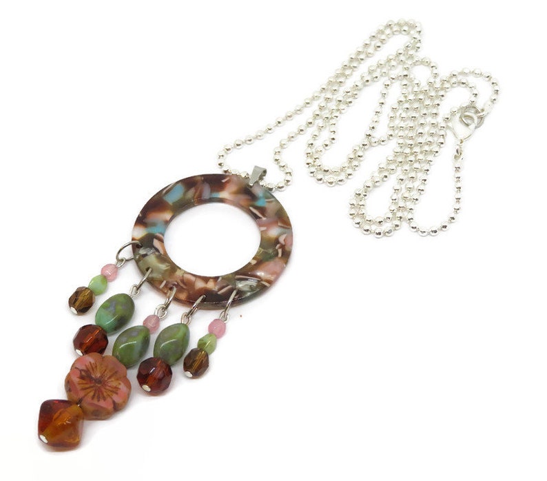 May include: A brown, green, and pink necklace with a round pendant and a silver chain. The pendant has a floral pattern and is accented with beads.