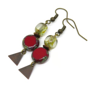 Op de afbeelding: Een paar oorhangers met rode en groene glazen kralen en bronzen driehoekige accenten.