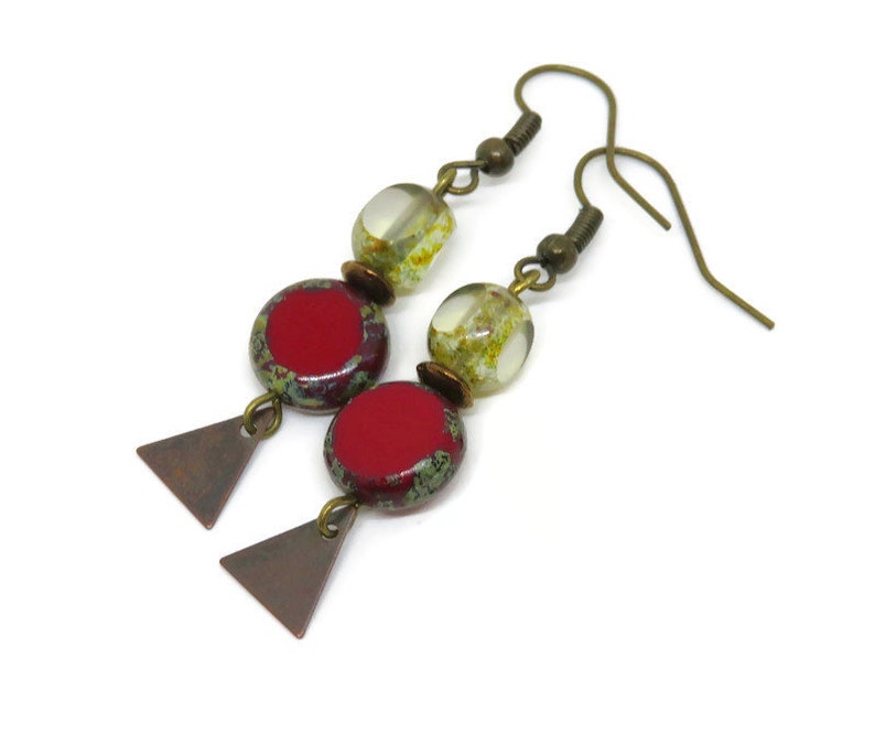 Op de afbeelding: Een paar oorhangers met rode en groene glazen kralen en bronzen driehoekige accenten.