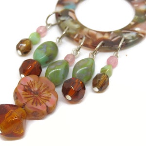 May include: A brown, green, and pink beaded dangle earring with a flower charm. The earring is made of glass beads and a metal hoop.