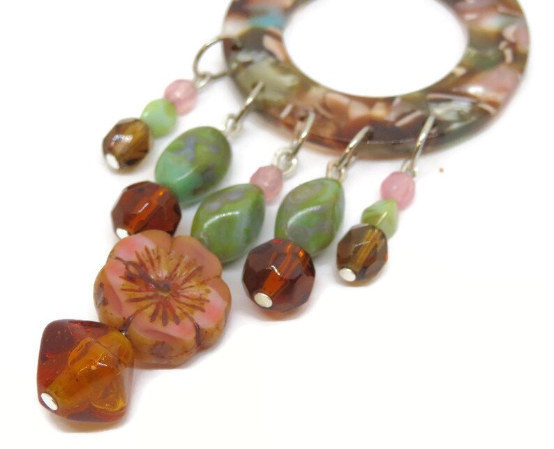 May include: A brown, green, and pink beaded dangle earring with a flower charm. The earring is made of glass beads and a metal hoop.