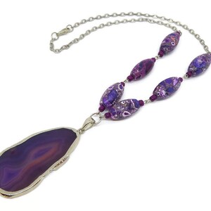 May include: A purple agate pendant necklace with a silver chain and purple and silver beads.